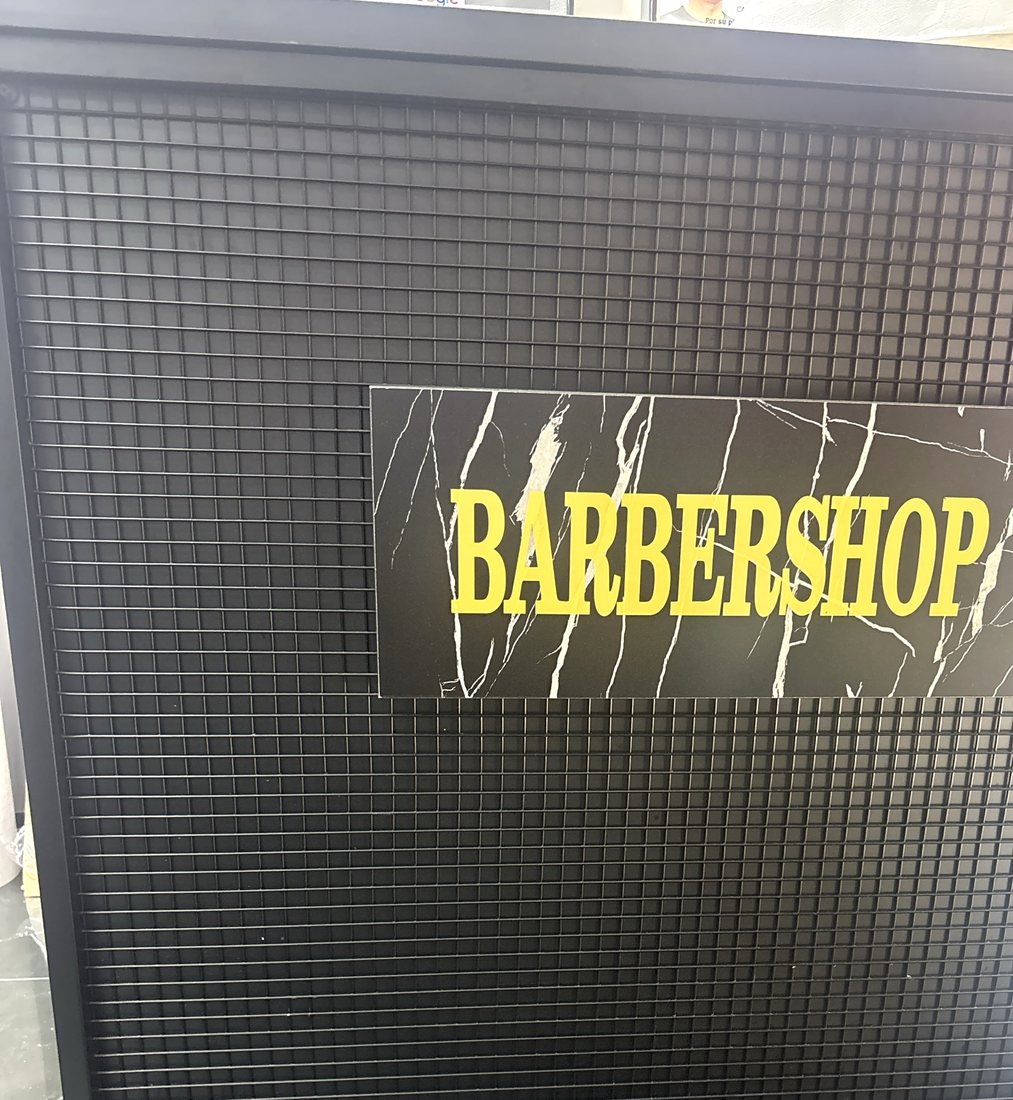 Rótulo BARBERSHOP en mármol negro sobre la pared de rejilla del local